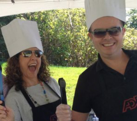 two ADP associates in chef hats and holding BBQ utensils