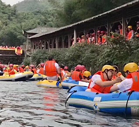 A large group of people rafting down the river wearing orange life vests and yellow and red helmets