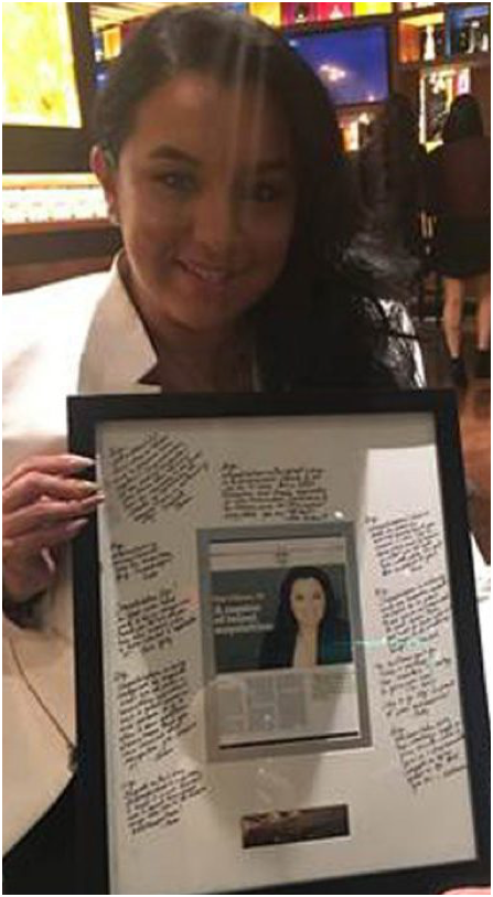 Gigi Alfonso holding a framed editorial article about herself