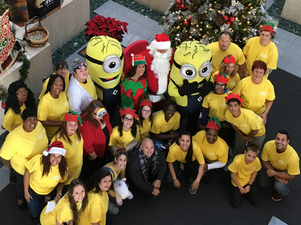large group of ADP associates wearing yellow T-shirts, standing around Santa Claus, an elf, and two minion characters from the movie 'Despicable Me.'