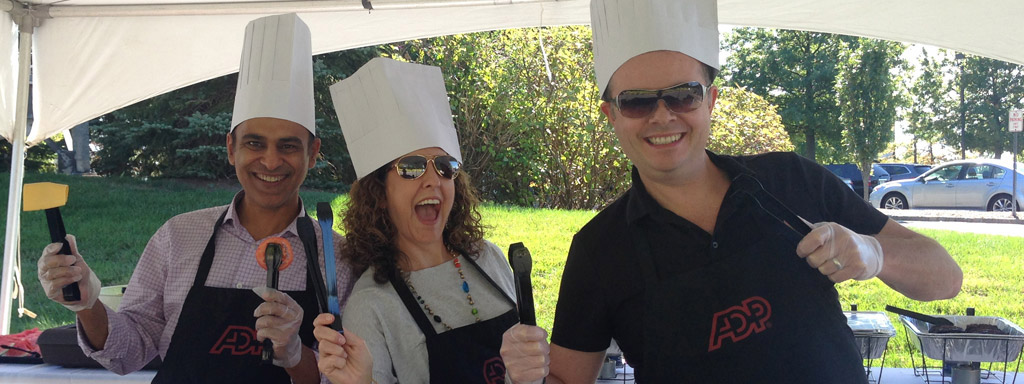 three ADP associates wearing chefs hats and holding BBQ utensils