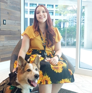 woman in yellow shirt and sunflower skirt sitting with hand on service dog beside her