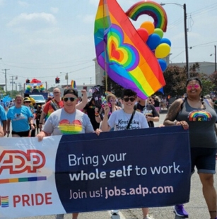 group pf people marching in a parage holding an ADP PRIDE banner.