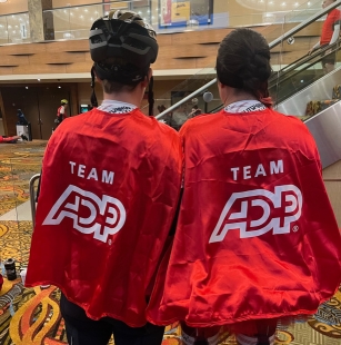 two people facing away, wearing red Team ADP capes