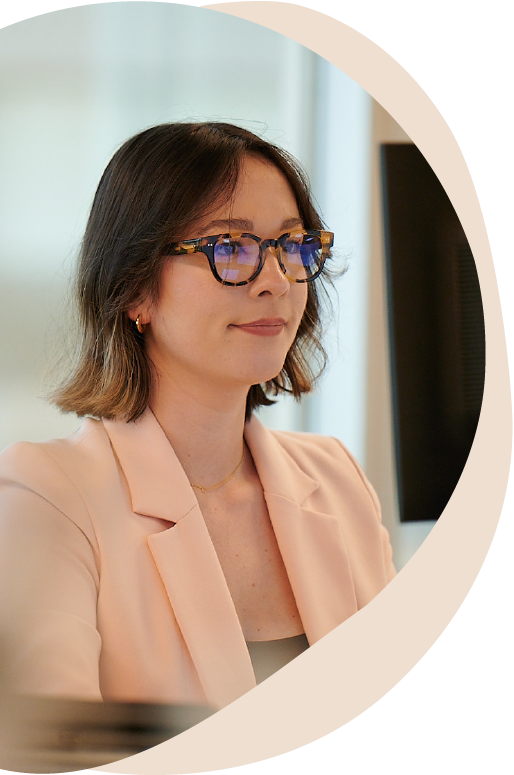 woman with short brown hair, glasses, and peach-color blazer looking at computer screen